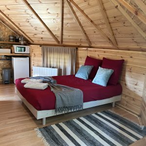 Cabane en bois dans le Pays de la Loire, lit douillet avec draps rouges et décor chaleureux.