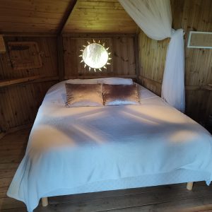Cabane en bois à Bourgogne, lit douillet avec miroir rond et lumière naturelle.