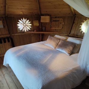 Cabane en bois à Bourgogne, lit douillet avec fenêtres décoratives en forme de fleurs.