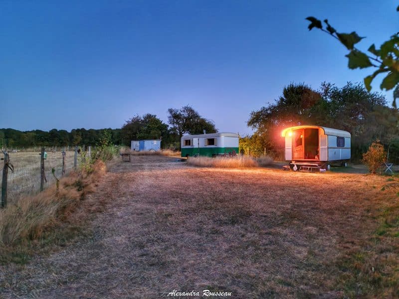 Charmant camping-car illuminé, entouré de champs dorés au crépuscule.