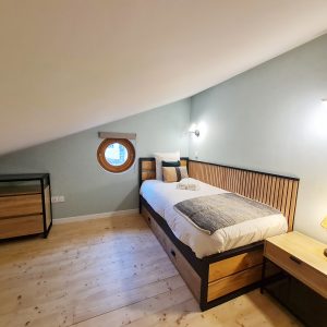Chambre cosy en bois avec fenêtre ronde, idéale pour un séjour insolite en Bourgogne-Franche-Comté.