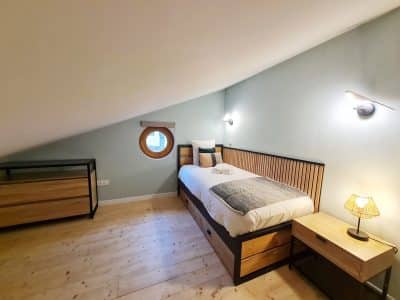 Chambre cosy en bois avec fenêtre ronde, idéale pour un séjour insolite en Bourgogne-Franche-Comté.