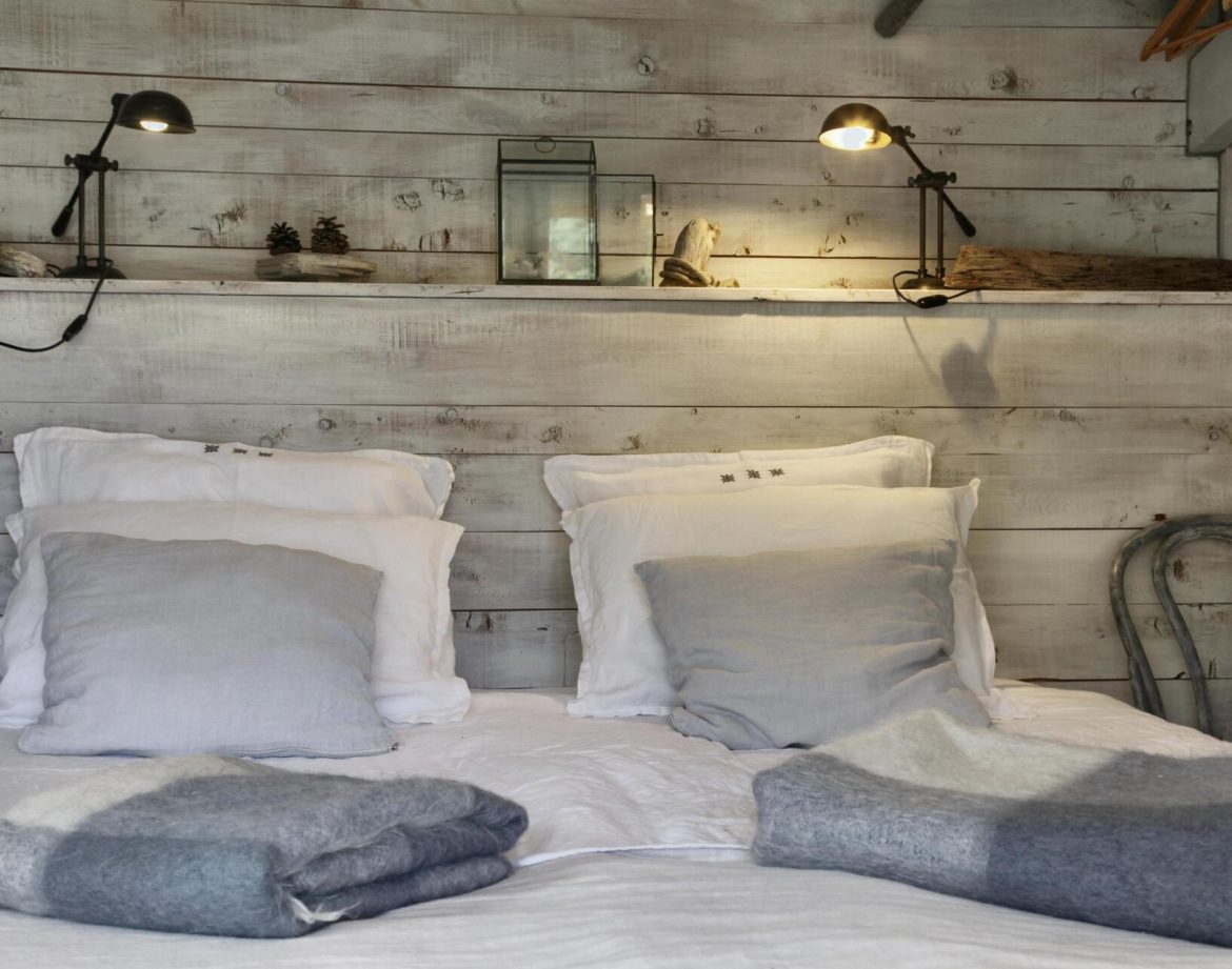 Chalet en bois avec lit douillet, décoré de coussins et lampes chaleureuses.