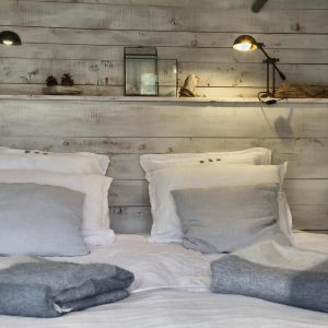 Chalet en bois avec lit douillet, décoré de coussins et lampes chaleureuses.