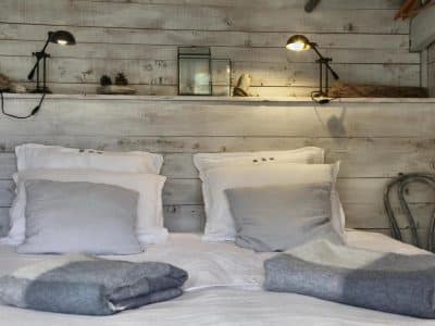 Chalet en bois avec lit douillet, décoré de coussins et lampes chaleureuses.