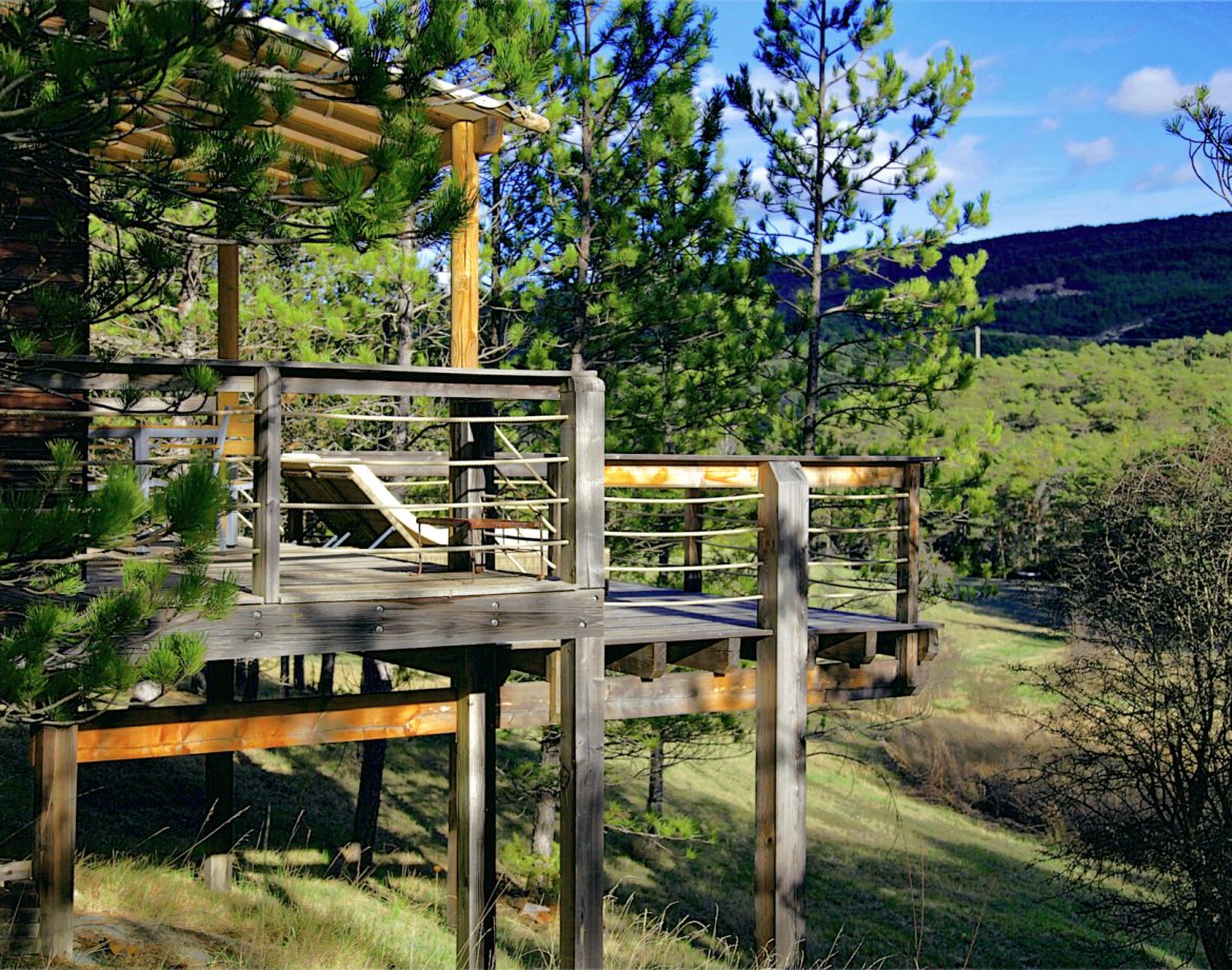 Cabane perchée en bois avec terrasse, entourée de verdure en Provence-Alpes-Côte dAzur.
