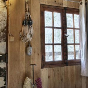 Cabane en bois avec fenêtre en bois, décorée de peaux et textiles colorés.