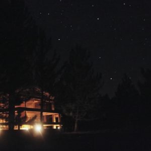 Cabane en bois sous un ciel étoilé, illuminée par des lanternes.