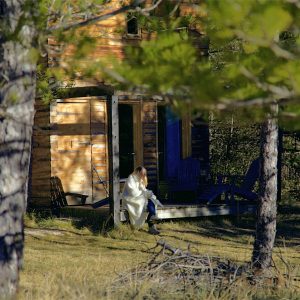 Cabane en bois dans la nature, avec une personne assise sur la terrasse.