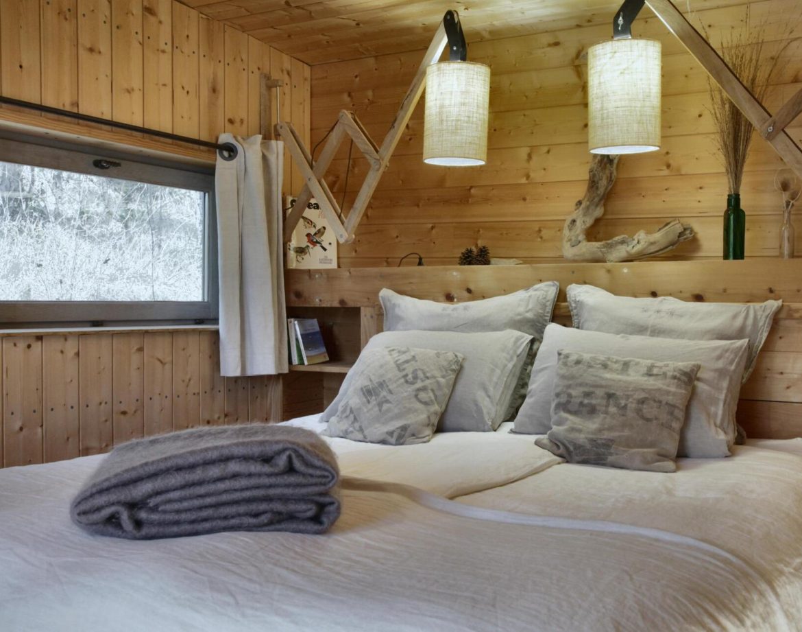 Chalet en bois chaleureux avec lit douillet et luminaires suspendus.
