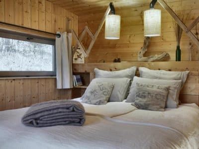 Chalet en bois chaleureux avec lit douillet et luminaires suspendus.