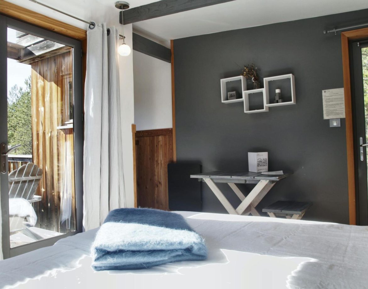 Chalet moderne en bois avec vue sur la nature, lit confortable et décor épuré.