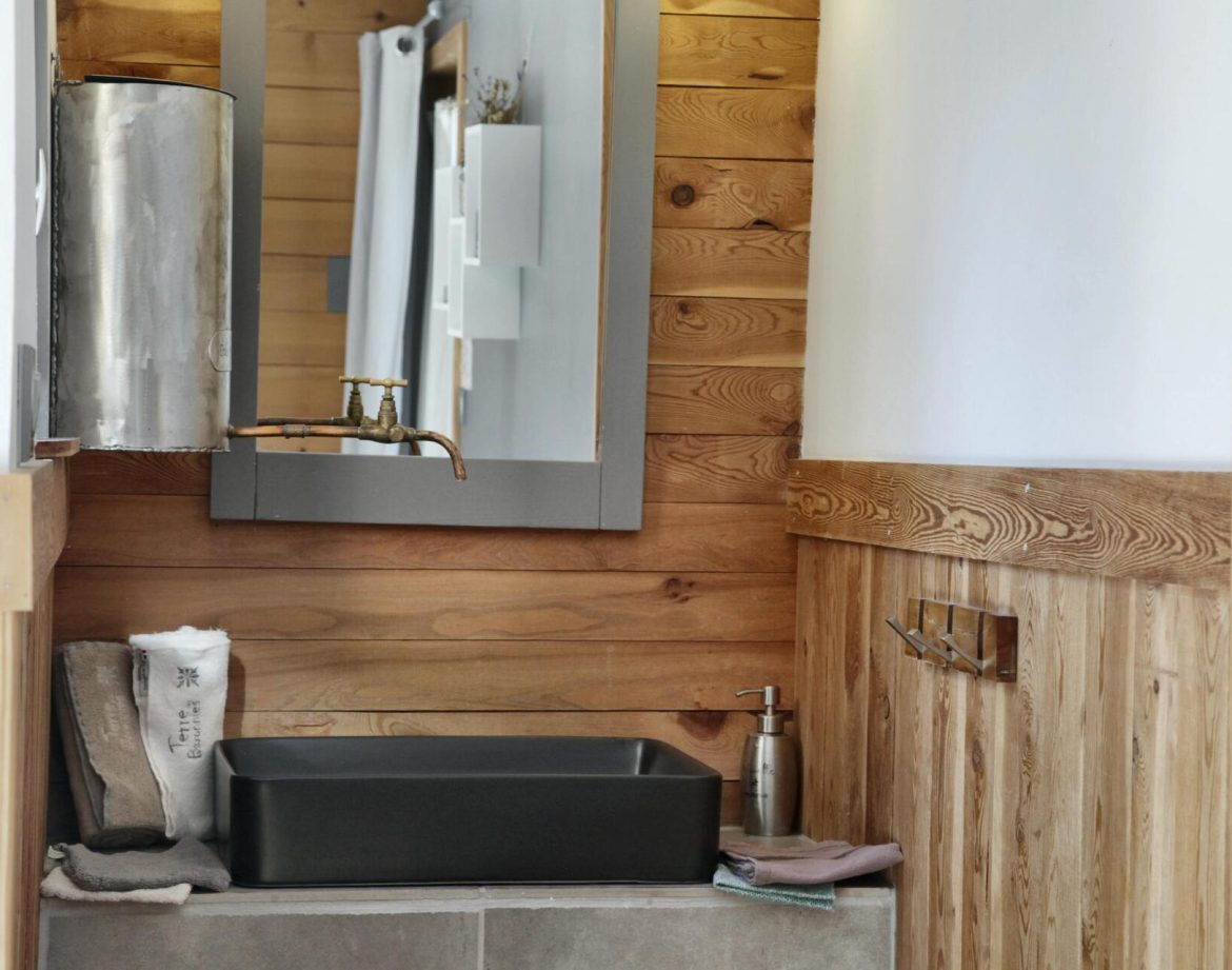 Salle de bain dun hébergement insolite en bois, avec un lavabo moderne et miroir.
