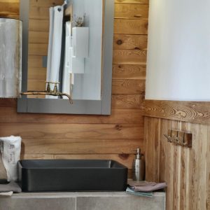 Salle de bain dun hébergement insolite en bois, avec un lavabo moderne et miroir.