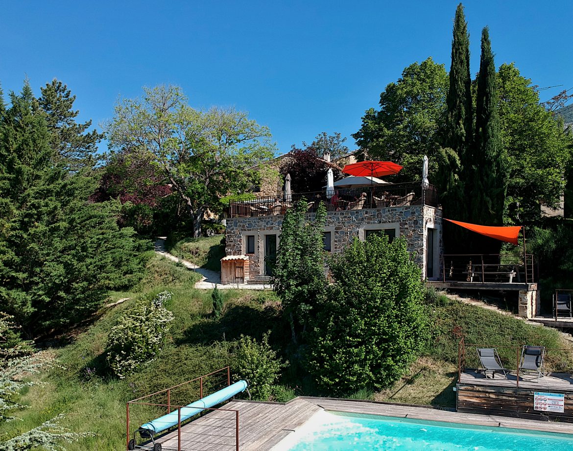 Hébergement insolite en pierre avec piscine, entouré de verdure et parasols colorés.