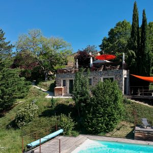 Hébergement insolite en pierre avec piscine, entouré de verdure et parasols colorés.