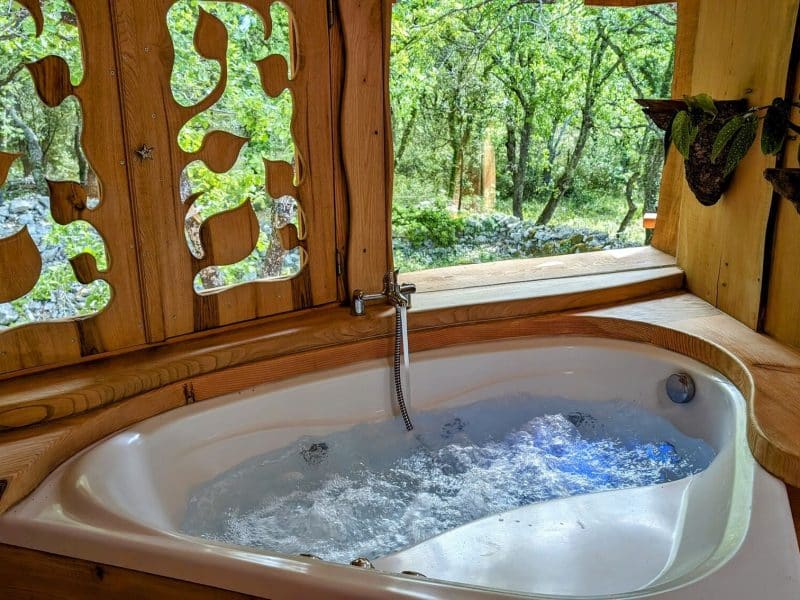 Baignoire relaxante dans une cabane en bois, entourée de verdure à Languedoc-Roussillon.