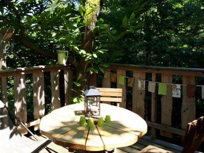 Cabane perchée en bois dans les arbres, avec une table ronde et des chaises.