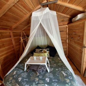 Cabane en bois avec lit douillet, drap en tulle et décoration naturelle.
