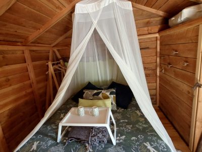 Cabane en bois avec lit douillet, drap en tulle et décoration naturelle.