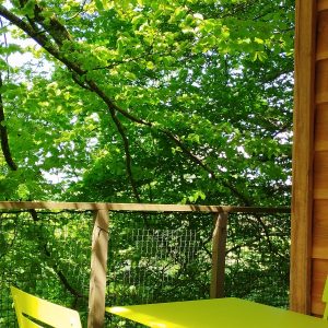 Cabane perchée à Grand-Est, avec terrasse et mobilier jaune vif entouré de verdure.