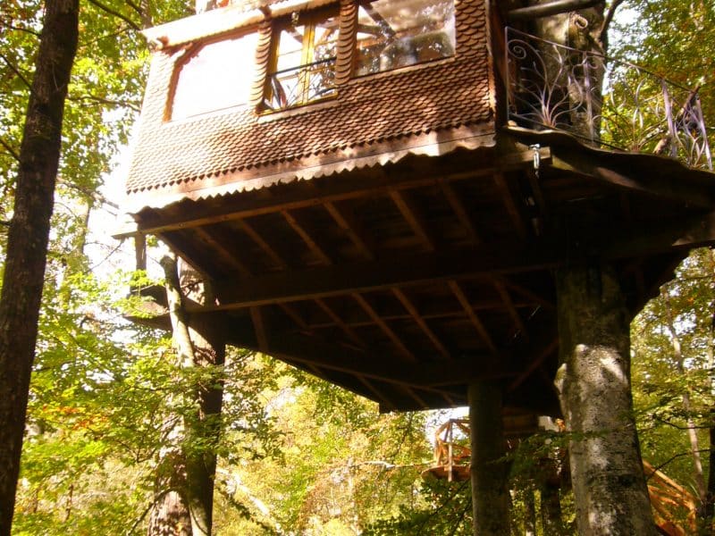 Cabane dans les arbres, perchée entre les feuillages, avec un balcon accueillant.