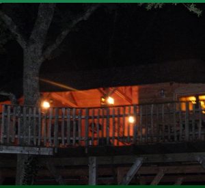 Cabane perchée au cœur de la nature, éclairée par des lanternes chaleureuses.