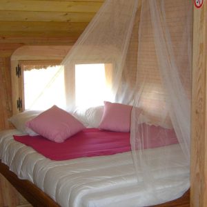 Cabane cosy avec lit à baldaquin et coussins roses, idéale pour un séjour romantique.