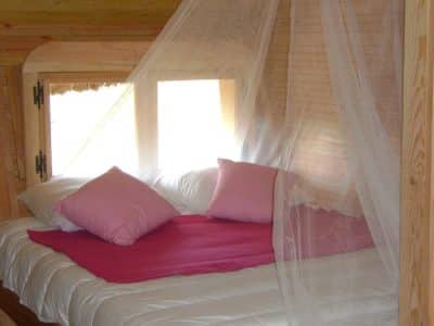 Cabane cosy avec lit à baldaquin et coussins roses, idéale pour un séjour romantique.