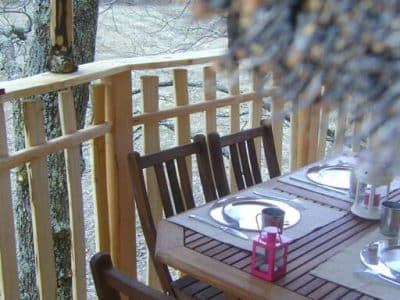 Cabane perchée avec terrasse en bois et table élégamment dressée.