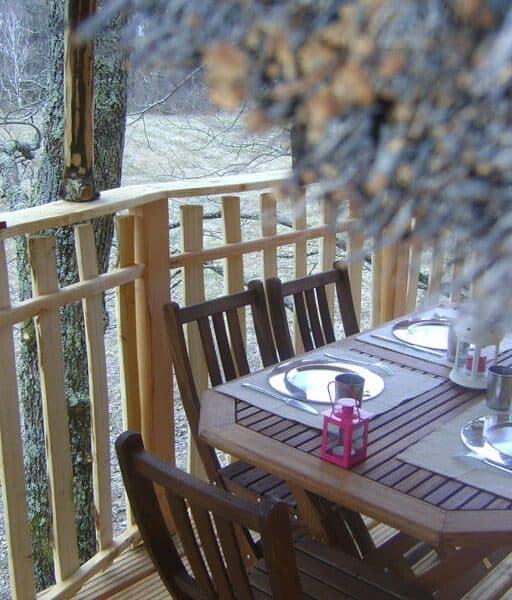 Cabane dans les arbres avec une terrasse en bois et une table prête pour le repas.