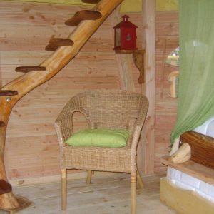 Hébergement insolite en bois avec une échelle en spirale et une chaise en osier.