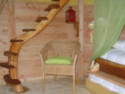 Hébergement insolite en bois avec une échelle en spirale et une chaise en osier.