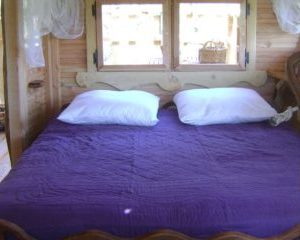 Chalet en bois avec lit double et draps violets, ambiance chaleureuse et naturelle.