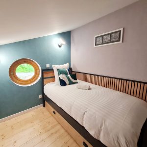 Chambre atypique en Bourgogne-Franche-Comté avec fenêtre ronde et décor moderne.