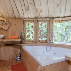 Cabane en bois avec baignoire balnéo et vue sur la nature verdoyante.