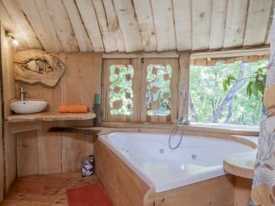 Cabane en bois avec baignoire balnéo et vue sur la nature verdoyante.