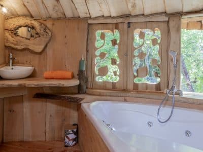 Cabane en bois avec baignoire, fenêtres sculptées et vue sur la nature.