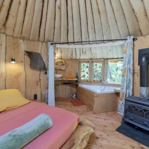 Cabane en bois avec lit coloré et baignoire, ambiance chaleureuse et naturelle.