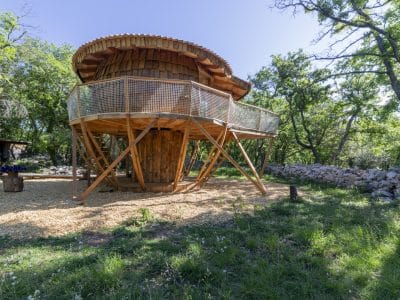 Cabane perchée en bois, entourée de verdure, avec une terrasse en bois spacieux.