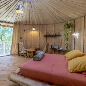 Hébergement insolite en yourte, intérieur en bois chaleureux avec lit coloré et vue sur la nature.