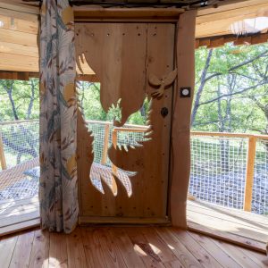Cabane perchée en bois avec une porte sculptée et vue sur la nature environnante.