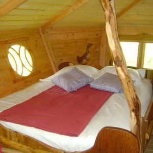 Cabane en bois avec lit douillet et fenêtres arrondies, ambiance chaleureuse.