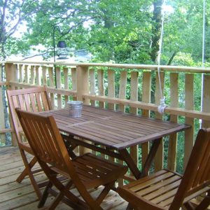 Cabane dans les arbres avec terrasse en bois et lanternes suspendues.