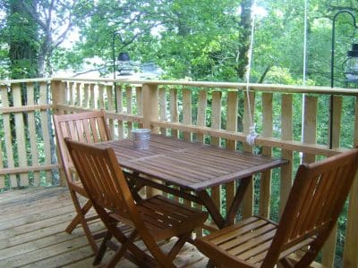 Cabane dans les arbres avec terrasse en bois et lanternes suspendues.