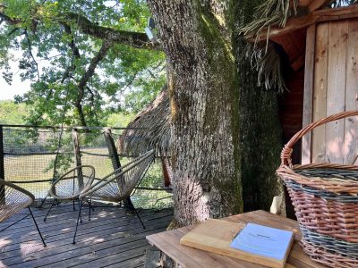Cabane perchée en bois, avec chaises en osier et vue sur la nature environnante.