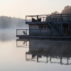 Cabane flottante au bord dun lac, entourée de brume matinale et dune vue apaisante.