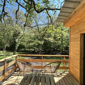 Cabane en bois avec terrasse, entourée de verdure en Auvergne-Rhône-Alpes.