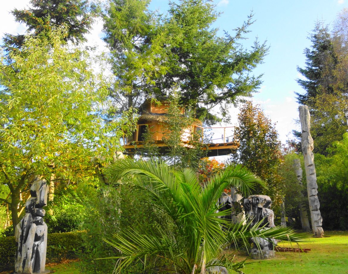 Cabane dans les arbres en Bretagne, entourée de sculptures et de verdure luxuriante.
