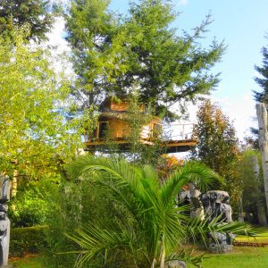 Cabane dans les arbres en Bretagne, entourée de sculptures et de verdure luxuriante.